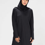 Woman wearing a long-sleeve black modest loose sports activewear top with a hijab on a white background, branded 'LUXE'.