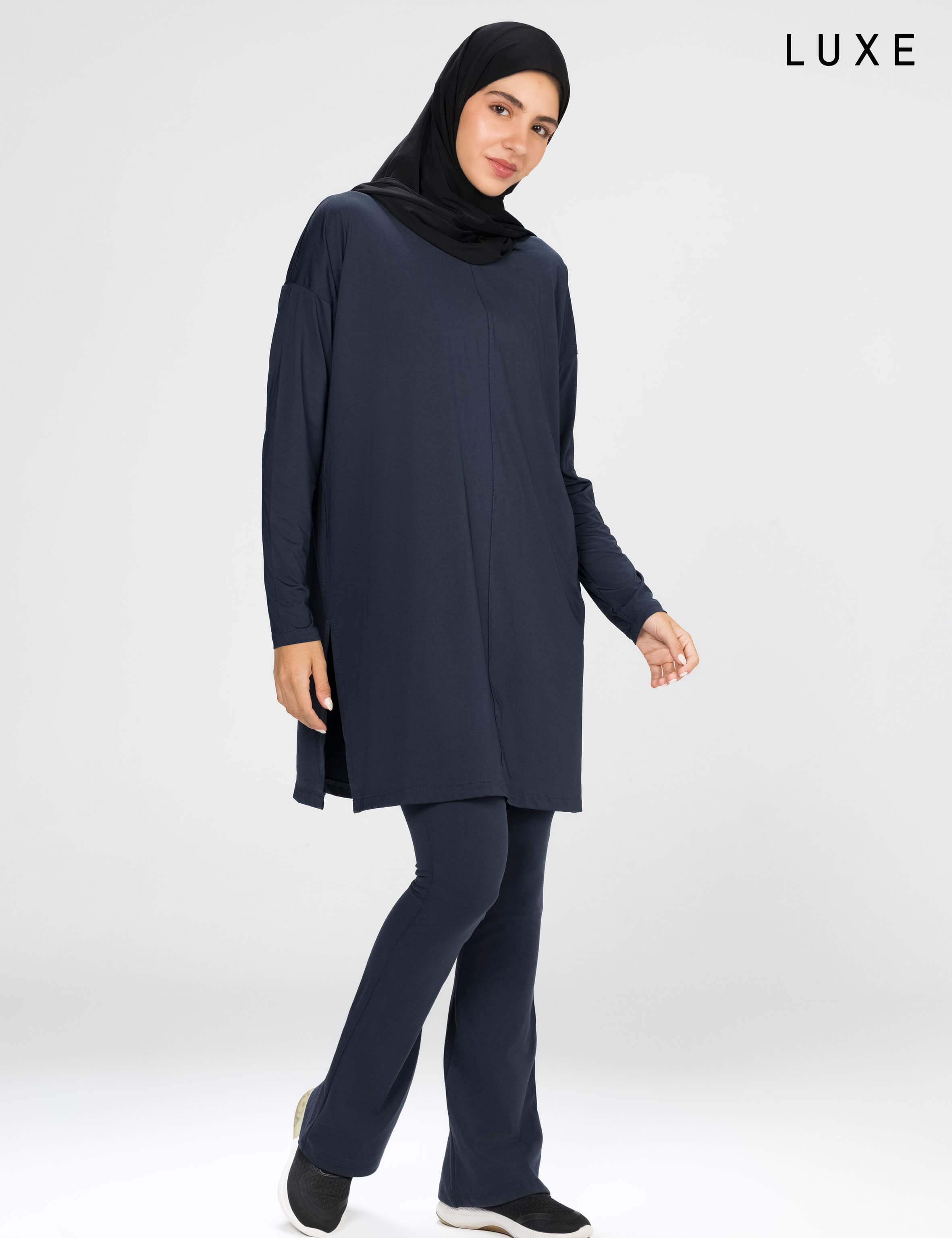 Woman wearing a long-sleeve navy modest loose sports activewear top with a hijab on a white background, branded 'LUXE'.