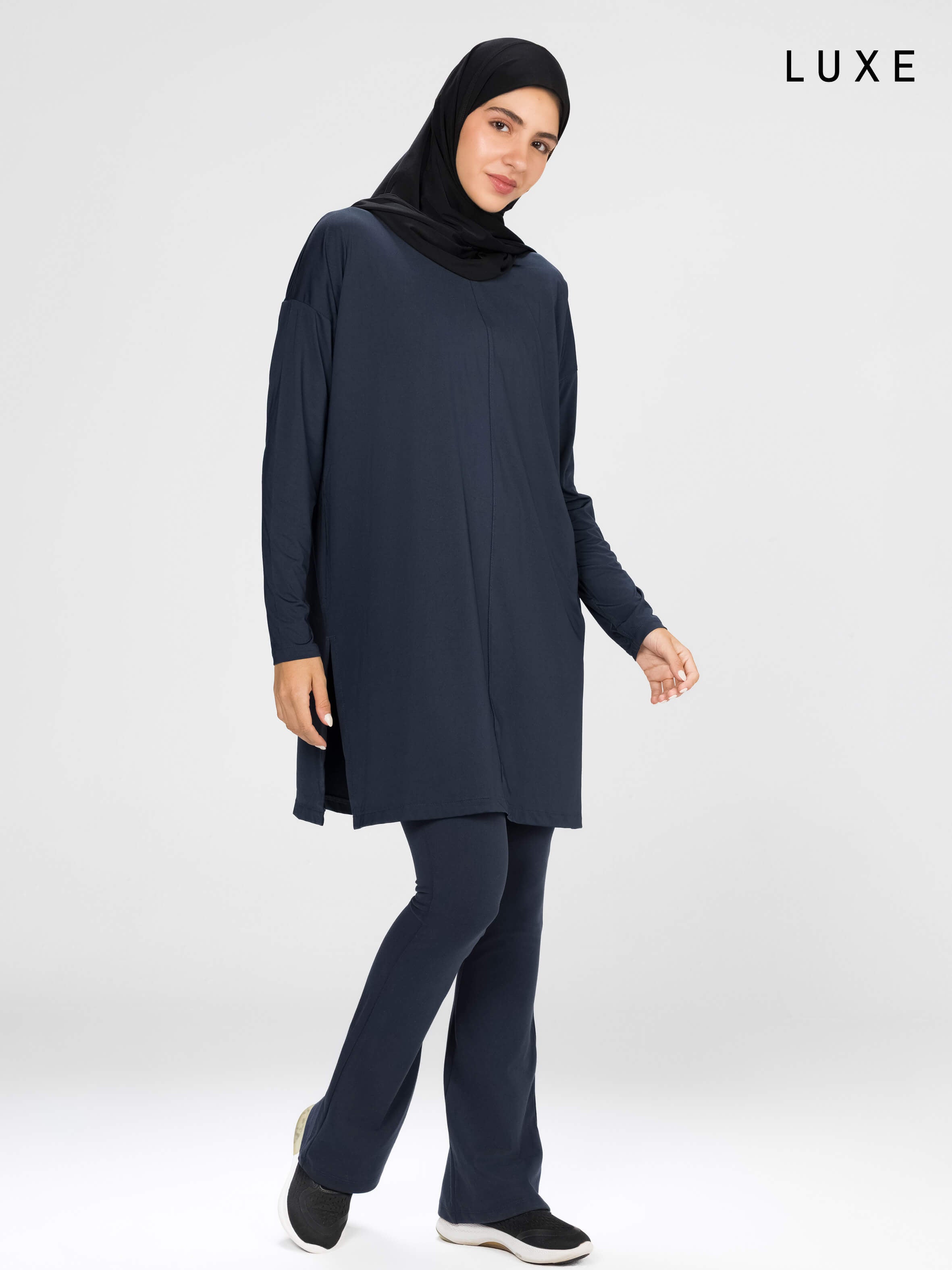 Woman wearing a long-sleeve navy modest loose sports activewear top with a hijab on a white background, branded 'LUXE'.
