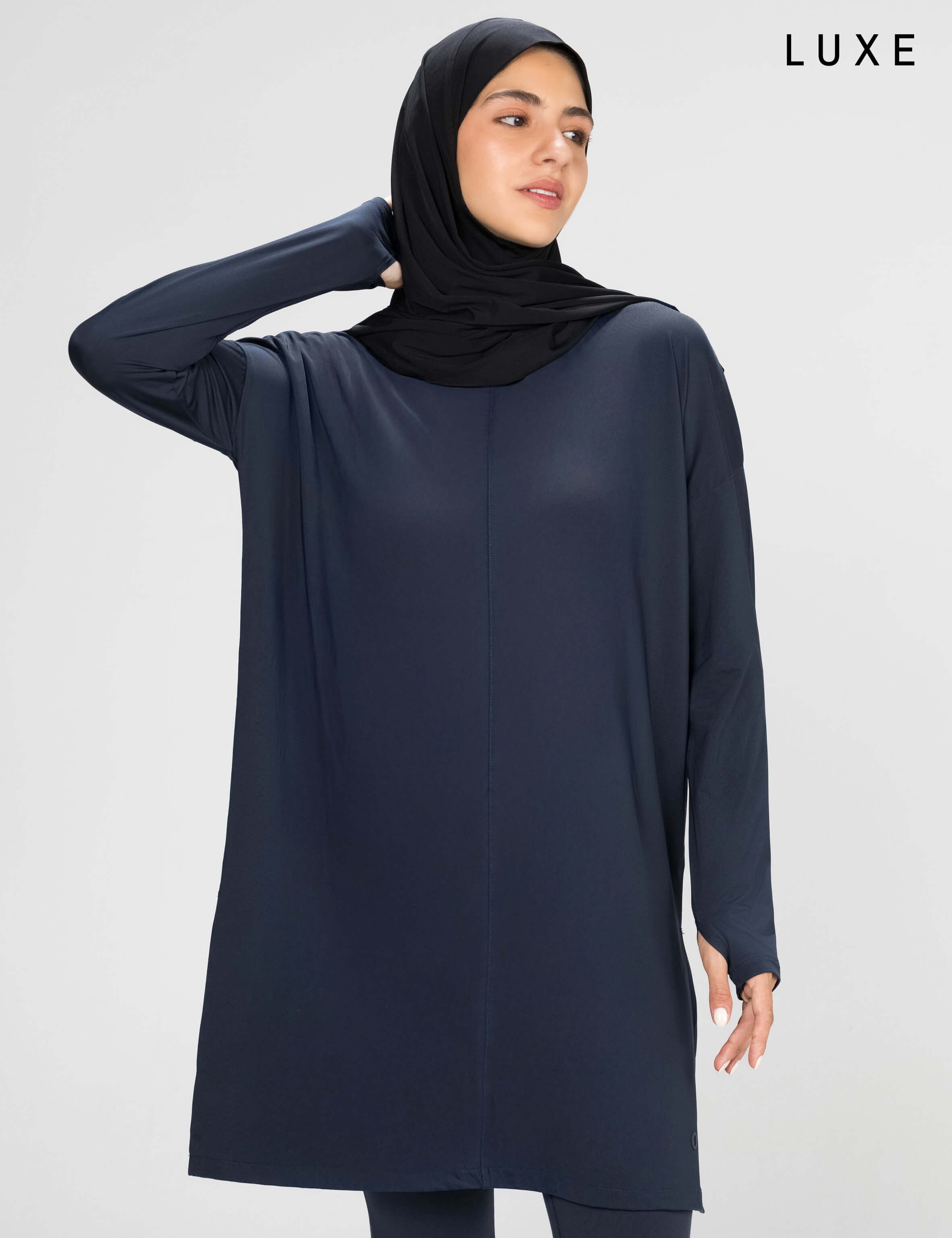 Woman wearing a long-sleeve navy modest loose sports activewear top with a hijab on a white background, branded 'LUXE'.