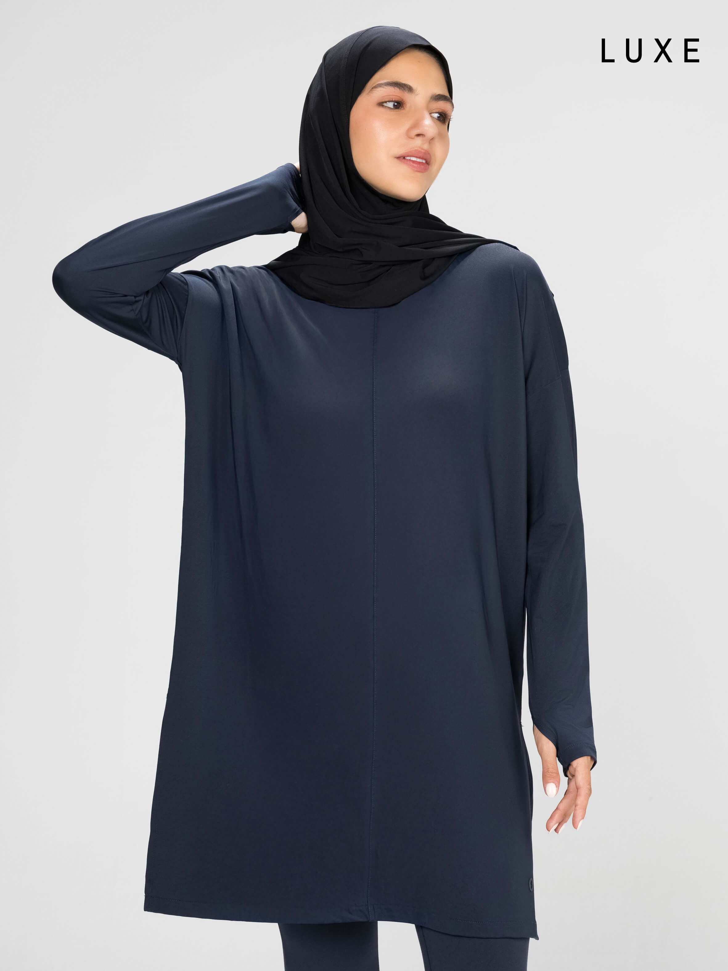 Woman wearing a long-sleeve navy modest loose sports activewear top with a hijab on a white background, branded 'LUXE'.