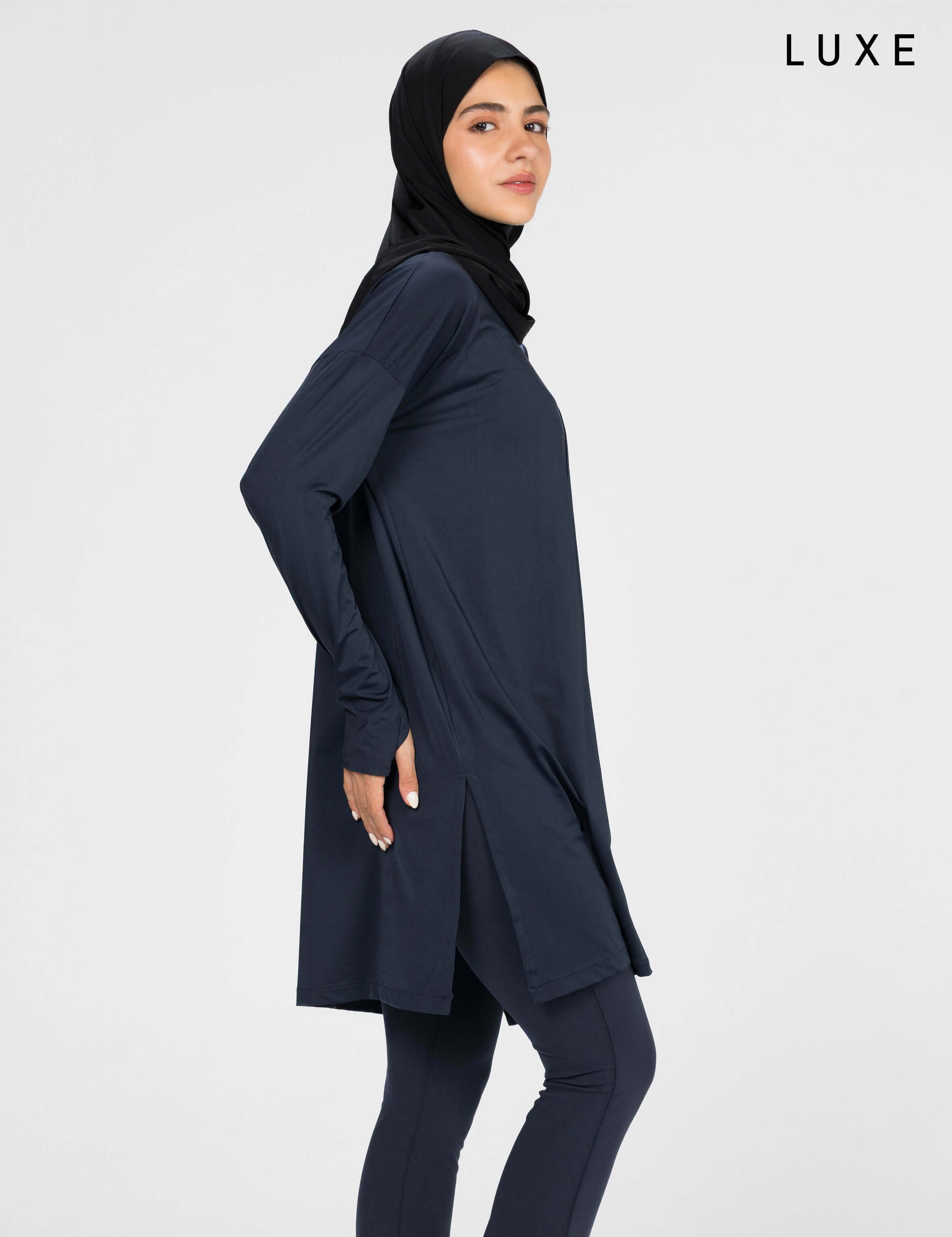 Woman wearing a long-sleeve navy modest loose sports activewear top with a hijab on a white background, branded 'LUXE'.