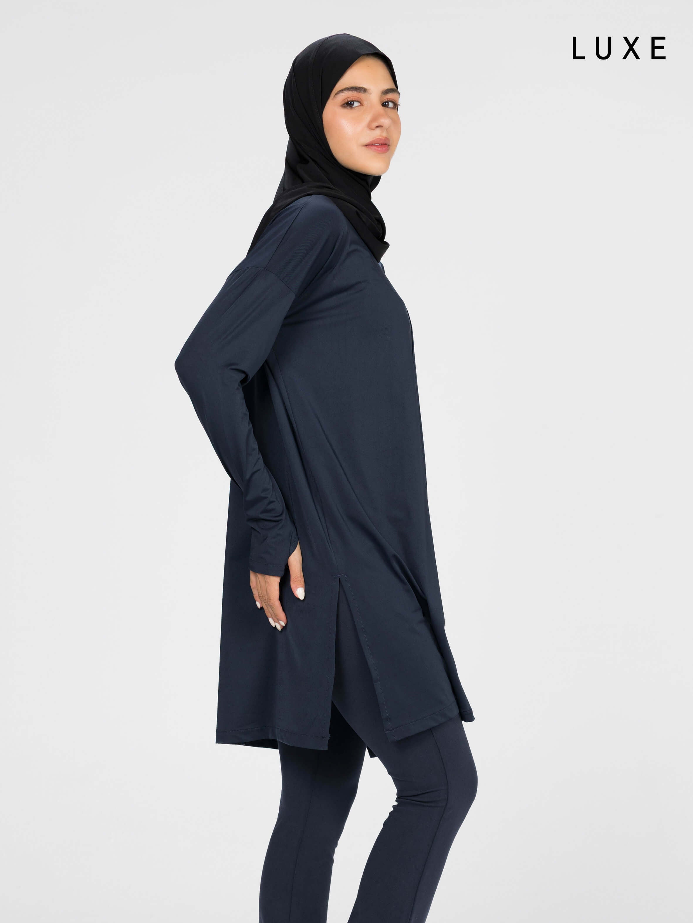 Woman wearing a long-sleeve navy modest loose sports activewear top with a hijab on a white background, branded 'LUXE'.