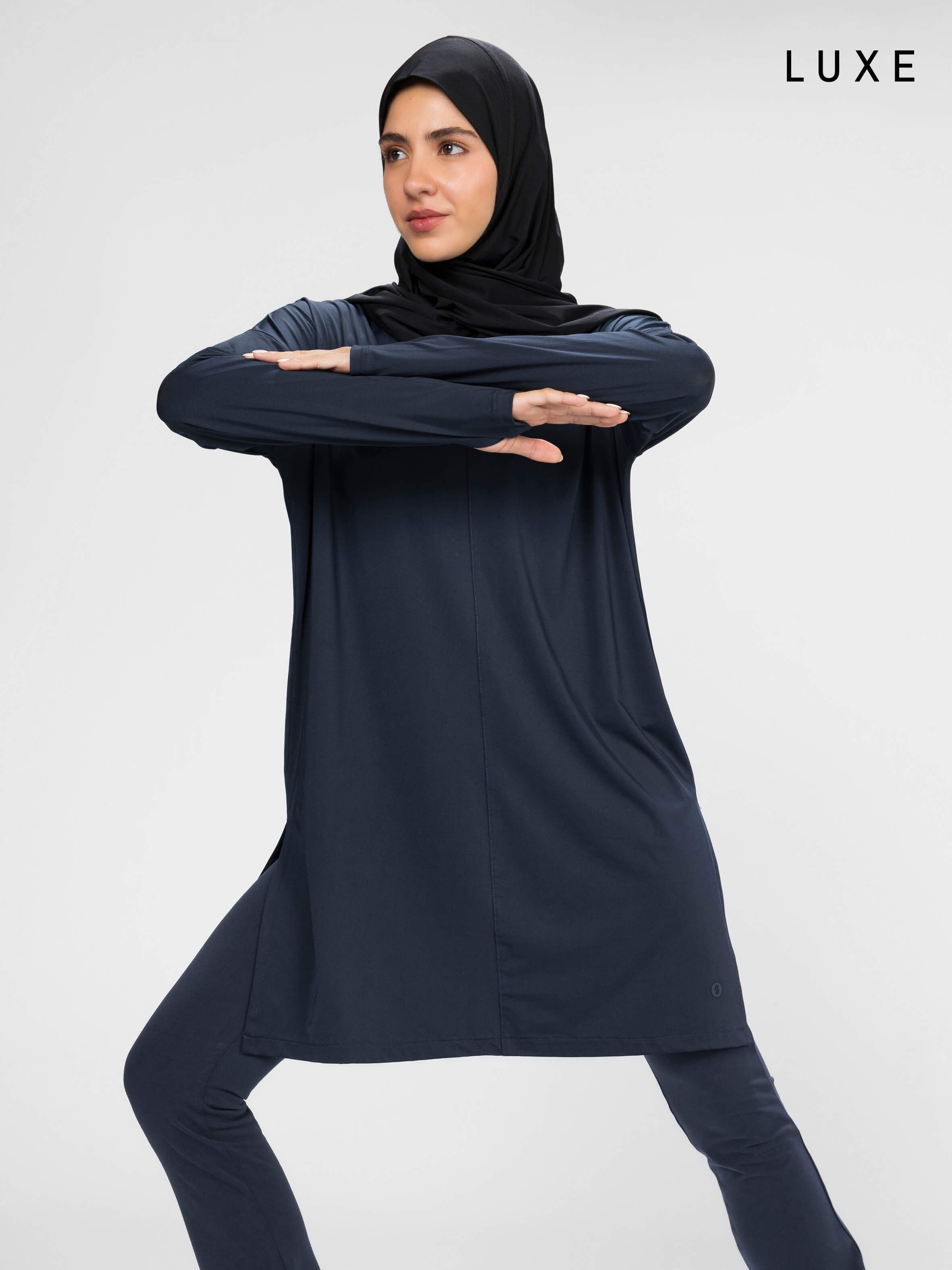 Woman wearing a long-sleeve navy modest loose sports activewear top with a hijab on a white background, branded 'LUXE'.