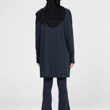 Woman wearing a long-sleeve navy modest loose sports activewear top with a hijab on a white background, branded 'LUXE'.