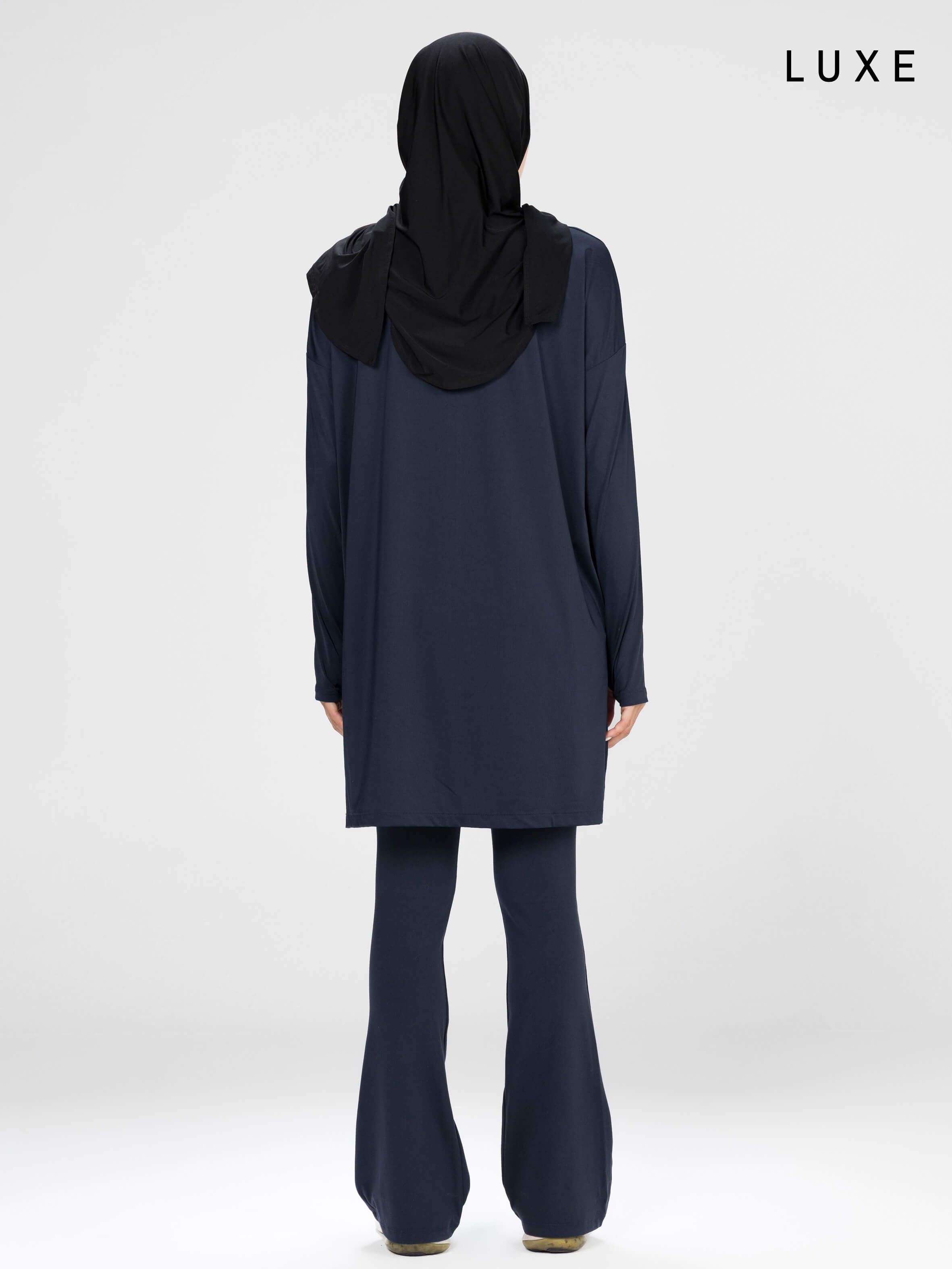 Woman wearing a long-sleeve navy modest loose sports activewear top with a hijab on a white background, branded 'LUXE'.