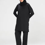 Woman wearing a long-sleeve black modest loose sports activewear top with a hijab on a white background, branded 'LUXE'.