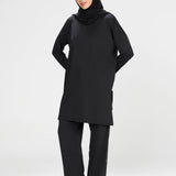 Woman wearing a long-sleeve black modest loose sports activewear top with a hijab on a white background, branded 'LUXE'.