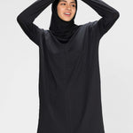 Woman wearing a long-sleeve black modest loose sports activewear top with a hijab on a white background, branded 'LUXE'.