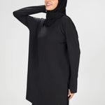 Woman wearing a long-sleeve black modest loose sports activewear top with a hijab on a white background, branded 'LUXE'.