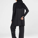 Woman wearing a long-sleeve black modest loose sports activewear top with a hijab on a white background, branded 'LUXE'.