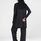 Woman wearing a long-sleeve black modest loose sports activewear top with a hijab on a white background, branded 'LUXE'.