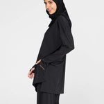 Woman wearing a long-sleeve black modest loose sports activewear top with a hijab on a white background, branded 'LUXE'.