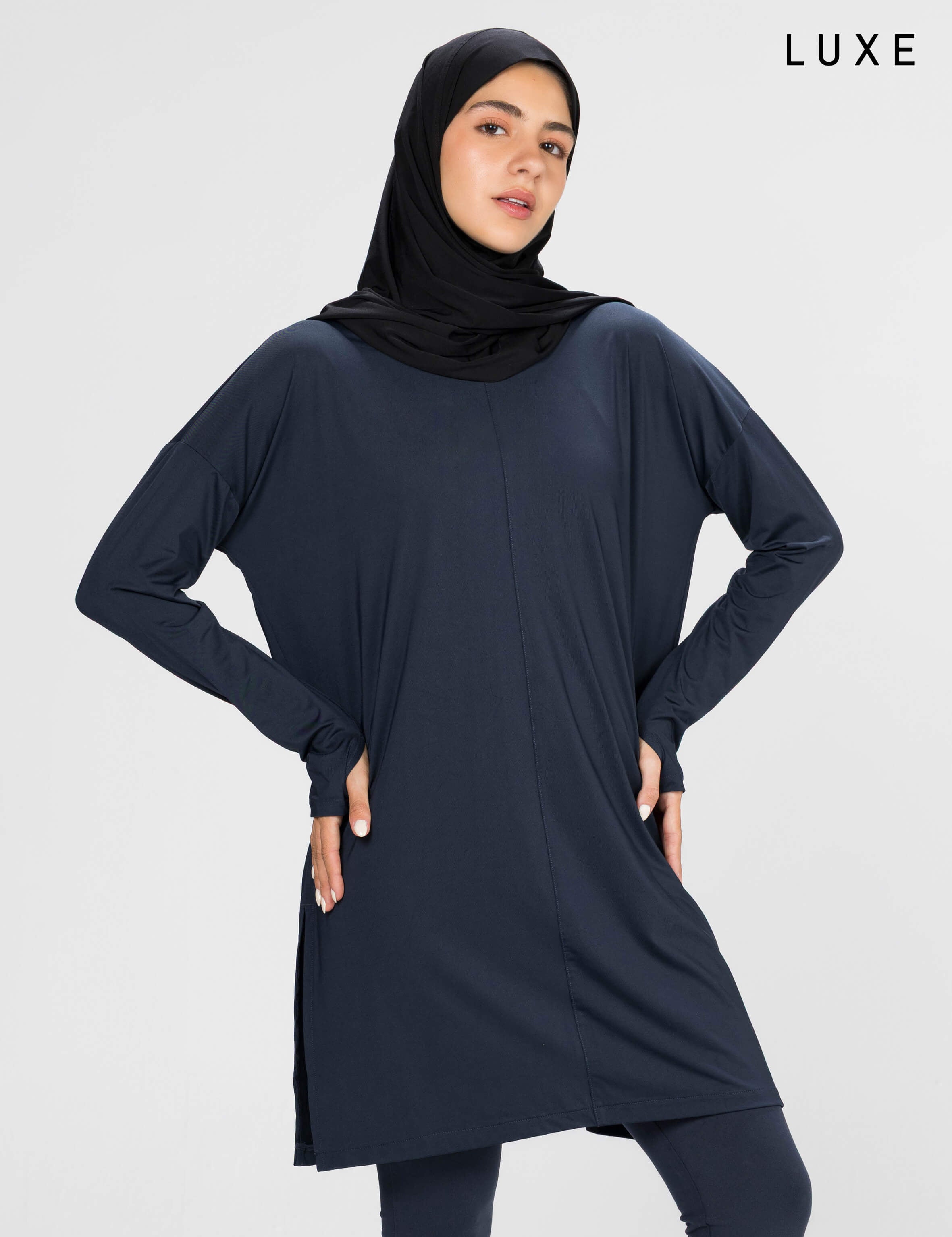 Woman wearing a long-sleeve navy modest loose sports activewear top with a hijab on a white background, branded 'LUXE'.