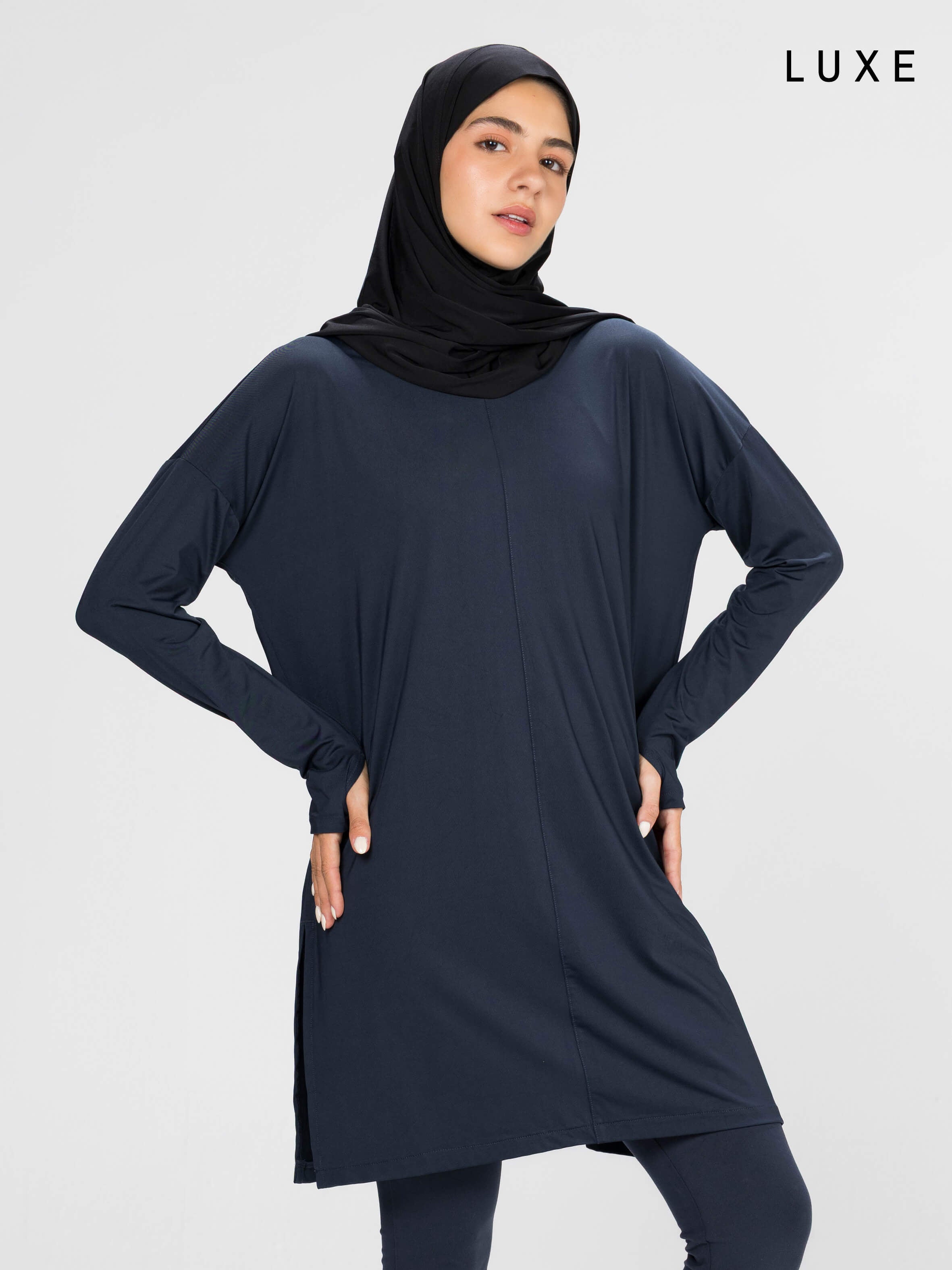 Woman wearing a long-sleeve navy modest loose sports activewear top with a hijab on a white background, branded 'LUXE'.